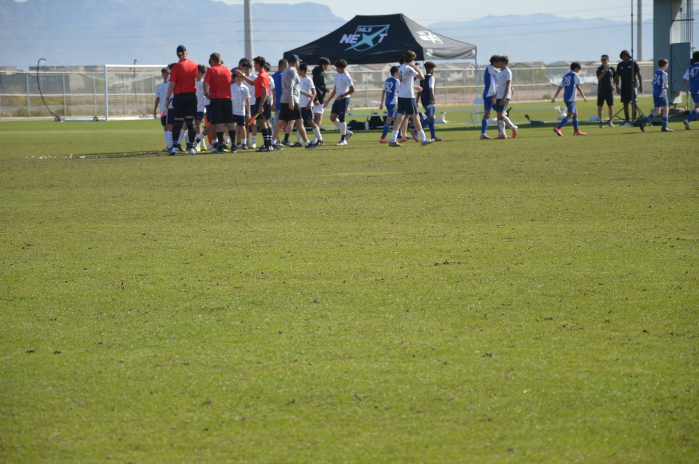 Soccer players and coaches gather by a tent on a field.